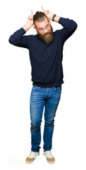 Fototapeta premium Young blond man wearing glasses and turtleneck sweater Posing funny and crazy with fingers on head as bunny ears, smiling cheerful