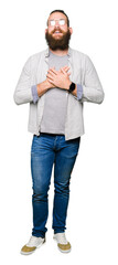 Young blond man wearing glasses smiling with hands on chest with closed eyes and grateful gesture...