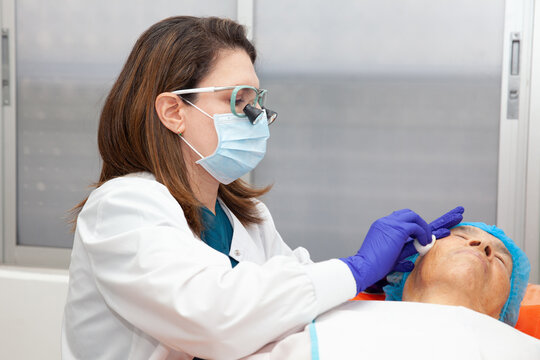 Dermatologist carrying out a skin biopsy on the face of a senior adult patient