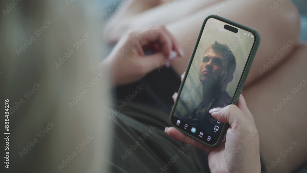 Poster caucasian woman scrolls through and watches app feed with short videos using mobile phone while lyin