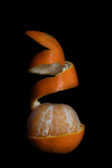 Close-up of a mandarin. The peel is half removed and stands out from the fruit in an upward spiral....