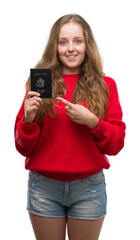 Young blonde woman holding passport of United States of America very happy pointing with hand and finger