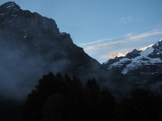 Mountains in the morning, Grindelwald, Switzerland. Sunrise in Swiss Alps. Snowy mountain peaks and morning fog in the forest