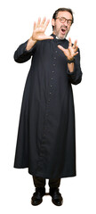 Middle age priest man wearing catholic robe afraid and terrified with fear expression stop gesture...