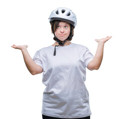 Young adult cyclist woman with down syndrome wearing safety helmet over isolated background clueless and confused expression with arms and hands raised. Doubt concept.