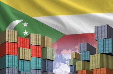 Comoros flag and big stack of shipping cargo containers in docks with sky background close up