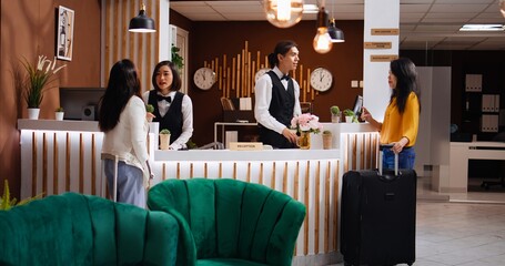 Asian women approach front desk to ask about their room, arriving at hotel from the airport and hoping for an early check in. Reception staff team greeting travelers and ensuring pleasant stay.