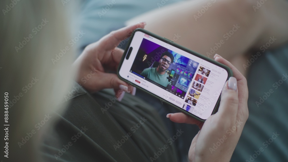 Poster close up of caucasian woman watching video about color grading using mobile phone while lying on sof