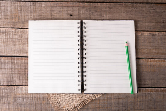 Spiral notebook with lined pages available and a green pencil on rustic wood.