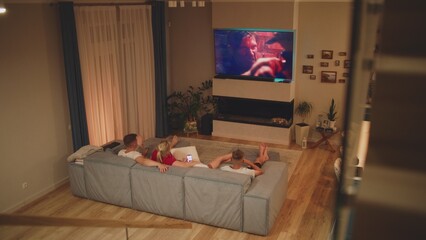 High angle of Caucasian family lying on sofa in cozy living room and watching action movie or TV...