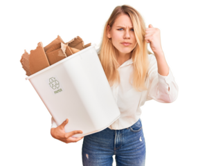 Young beautiful blonde woman holding recycle paper bin annoyed and frustrated shouting with anger, yelling crazy with anger and hand raised