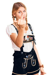 Young beautiful blonde woman wearing oktoberfest dress showing middle finger, impolite and rude...