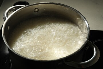 Boiling rice in metal pot on stove, closeup