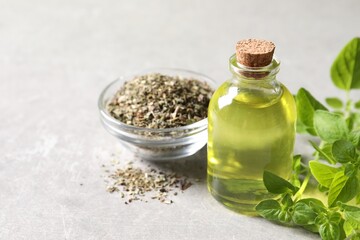 Essential oil in bottle, dry herb and oregano leaves on light grey textured table, closeup. Space for text