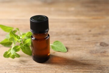 Essential oil in bottle and oregano twigs on wooden table, closeup. Space for text