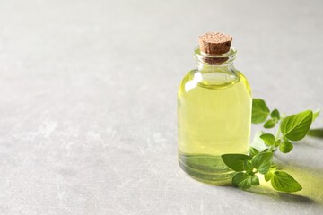 Essential oil in bottle and oregano twig on light grey textured table, closeup. Space for text