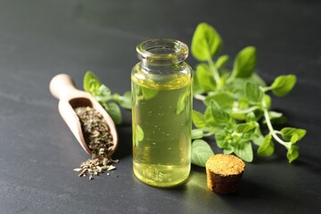 Essential oil in bottle, scoop with dry herb and oregano twigs on dark textured table, closeup