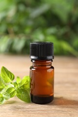 Essential oil in bottle and oregano twigs on wooden table against blurred green background, closeup