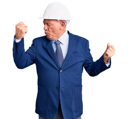 Senior handsome grey-haired man wearing suit and architect hardhat showing arms muscles smiling proud. fitness concept.