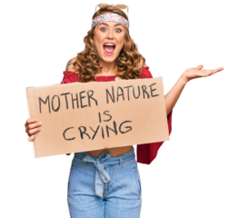 Young blonde girl wearing hippie style holding mother nature is crying protest cardboard banner celebrating victory with happy smile and winner expression with raised hands
