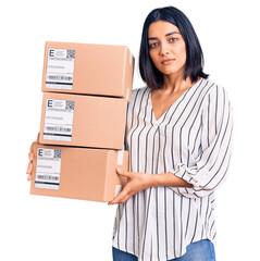 Young beautiful latin woman holding delivery package thinking attitude and sober expression looking self confident