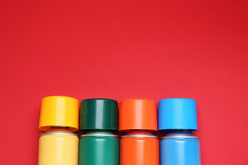 Many spray paint cans on red background, top view. Space for text