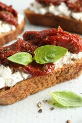 Delicious ricotta bruschetta with sun dried tomatoes and basil on plate, closeup
