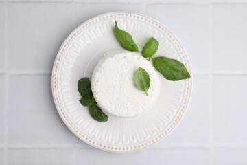 Fresh ricotta (cream cheese) and basil on light tiled table, top view