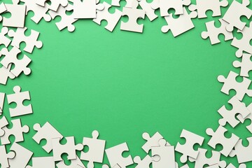 Frame of white puzzle pieces on green background, top view. Space for text