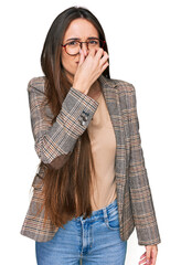 Young hispanic girl wearing business clothes and glasses smelling something stinky and disgusting,...