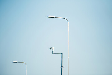 Defocused daytime image of tall, minimalistic street lamps and a security camera against a clear...