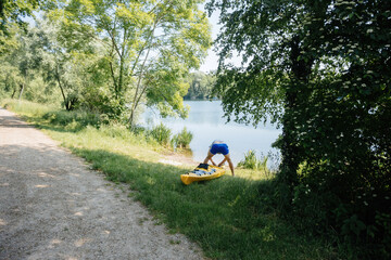 Unrecognizable person preparing a yellow kayak by a calm lake, surrounded by lush greenery and trees, highlighting outdoor activity and nature's beauty in a serene setting