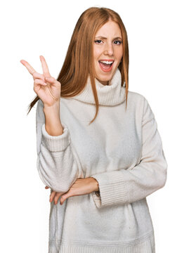 Young irish woman wearing casual winter sweater smiling with happy face winking at the camera doing victory sign with fingers. number two.