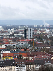 Obraz premium A detailed aerial view of Freiburg, highlighting the city's diverse architecture, residential areas, and distant mountains under a cloudy sky.