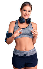 Young beautiful hispanic woman wearing gym clothes and using headphones disgusted expression, displeased and fearful doing disgust face because aversion reaction. with hands raised