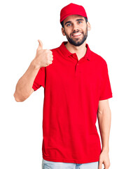 Young handsome man with beard wearing delivery uniform doing happy thumbs up gesture with hand. approving expression looking at the camera showing success.