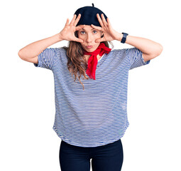 Young beautiful blonde woman wearing french beret and striped t-shirt trying to open eyes with fingers, sleepy and tired for morning fatigue