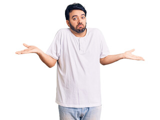 Young hispanic man wearing casual clothes clueless and confused expression with arms and hands...