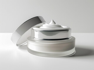 glass jar of beauty cream with silver lid resting on the side and reflected in the white plane