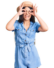 Brunette teenager girl wearing summer hat doing ok gesture like binoculars sticking tongue out, eyes looking through fingers. crazy expression.