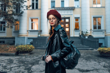 Stylish woman in glasses and red beret standing confidently in front of a historic brick building