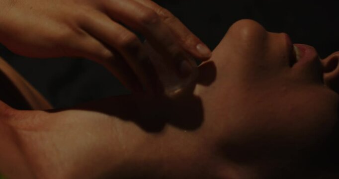 A hand sensually rubs an ice cube on the neck of a beautiful woman dressed in lingerie