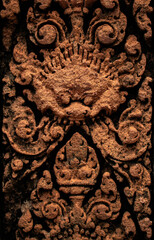 Detailed carved bas relief in red sandstone of mythological Kala at Banteay Srei -citadel of women and beauty- Hindu Temple dedicated to god Shiva and Parvati, Siem Reap, Cambodia.