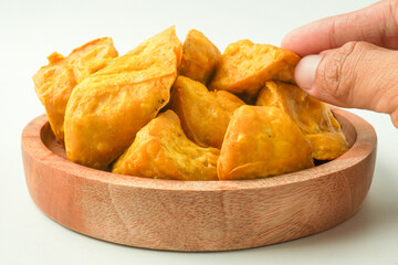Someone hand is picking fried yellow tofu on wooden plate. Tahu Takwa is a specialty food from Kediri, East Java, Indonesia. Flat Lay Photo