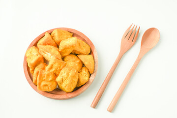 Flat Lay Photo of Fried yellow tofu served on wooden plate next to wooden spoon and fork. Tahu Takwa is a specialty food from Kediri, East Java, Indonesia. Concept for Plant based protein.