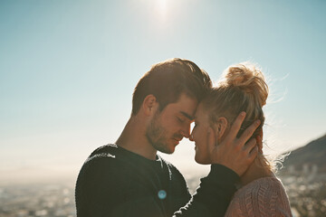 Happy couple, forehead and touching with blue sky on mountain for love, support or embrace in nature. Young man and woman for affection, care or trust on outdoor holiday, weekend or relief together