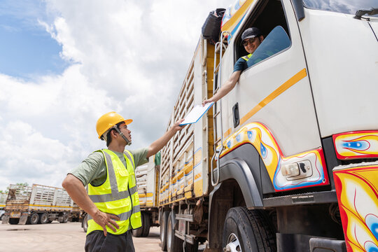 Asian professional truck driver in a high-visibility vest, checking documents and paperwork while standing beside a large cargo truck, transport business.