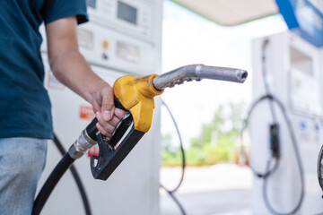 Close up hand of A male holding a fuel nozzle against with gas station blurred background.