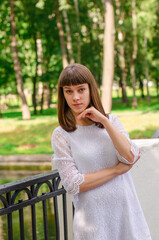 A woman in a white dress stands on a bridge. She is wearing black heels and has her hands on her hips. Concept of elegance and sophistication, as the woman is dressed in a formal outfit