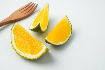 Three slices of fresh green colored orange (citrus sinensis) next to wooden fork isolated on white background.